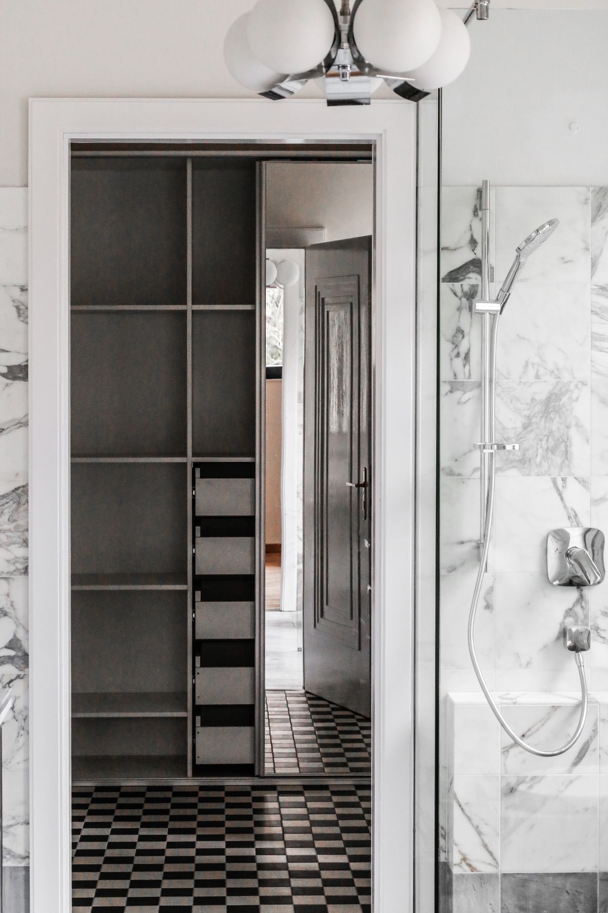 Marble-clad bath with dark panelled door, checkered tile floor, and chrome shower.