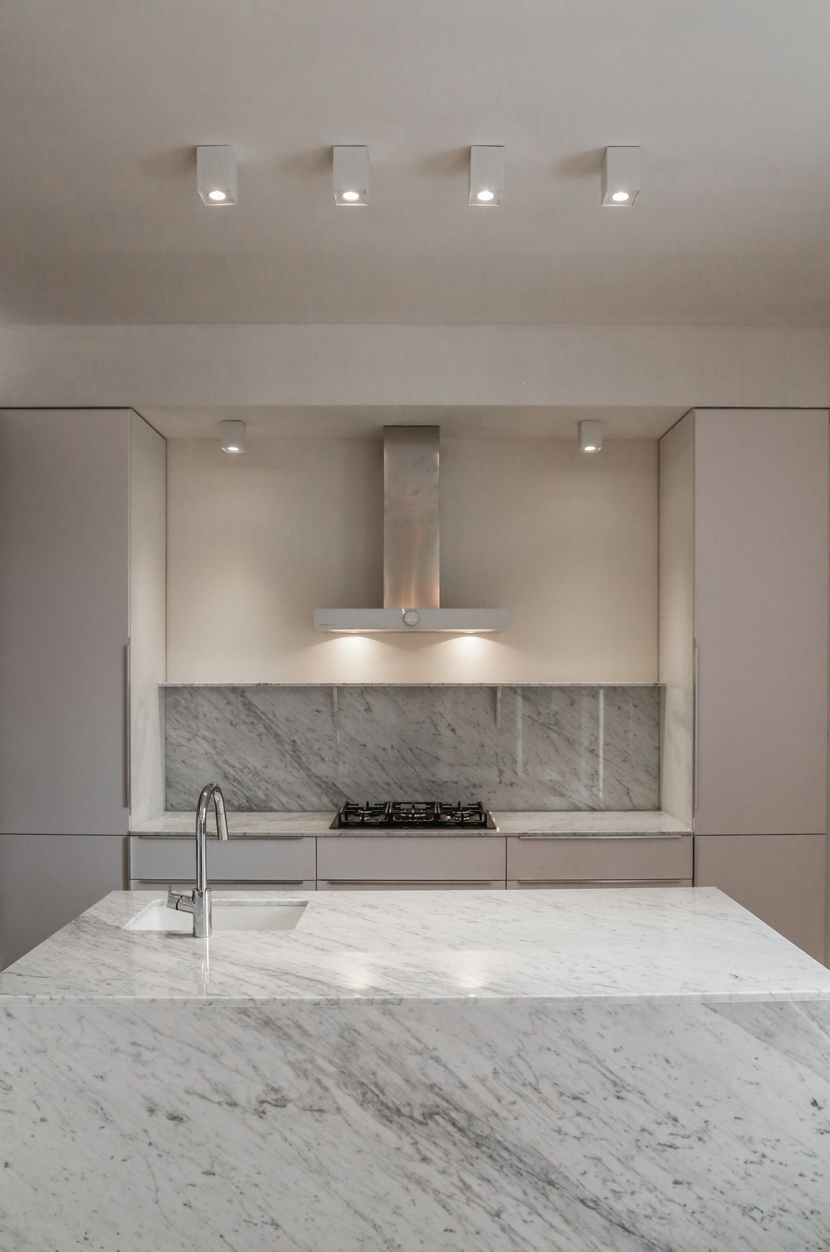 Minimal marble kitchen with island, recessed ceiling spots, and stainless range hood.