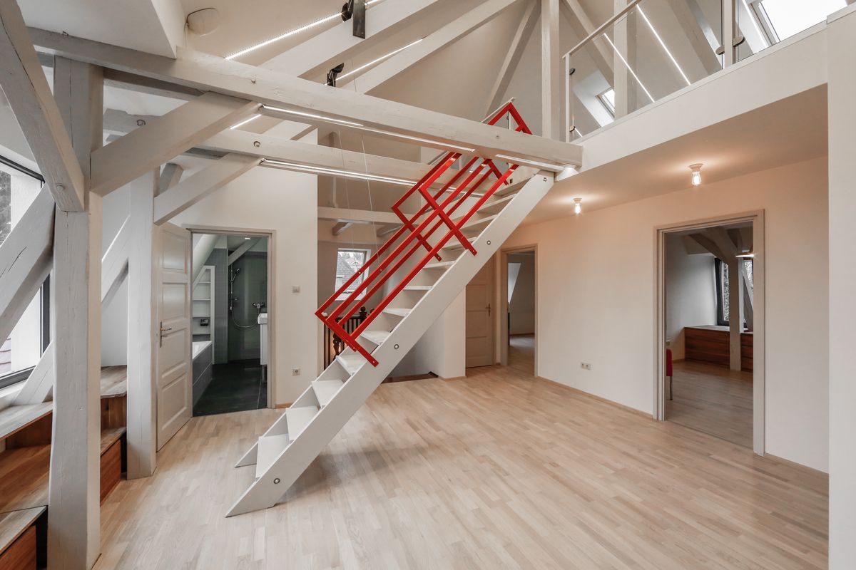 Attic loft with white-painted beams, red metal staircase railing, and pale timber floor.